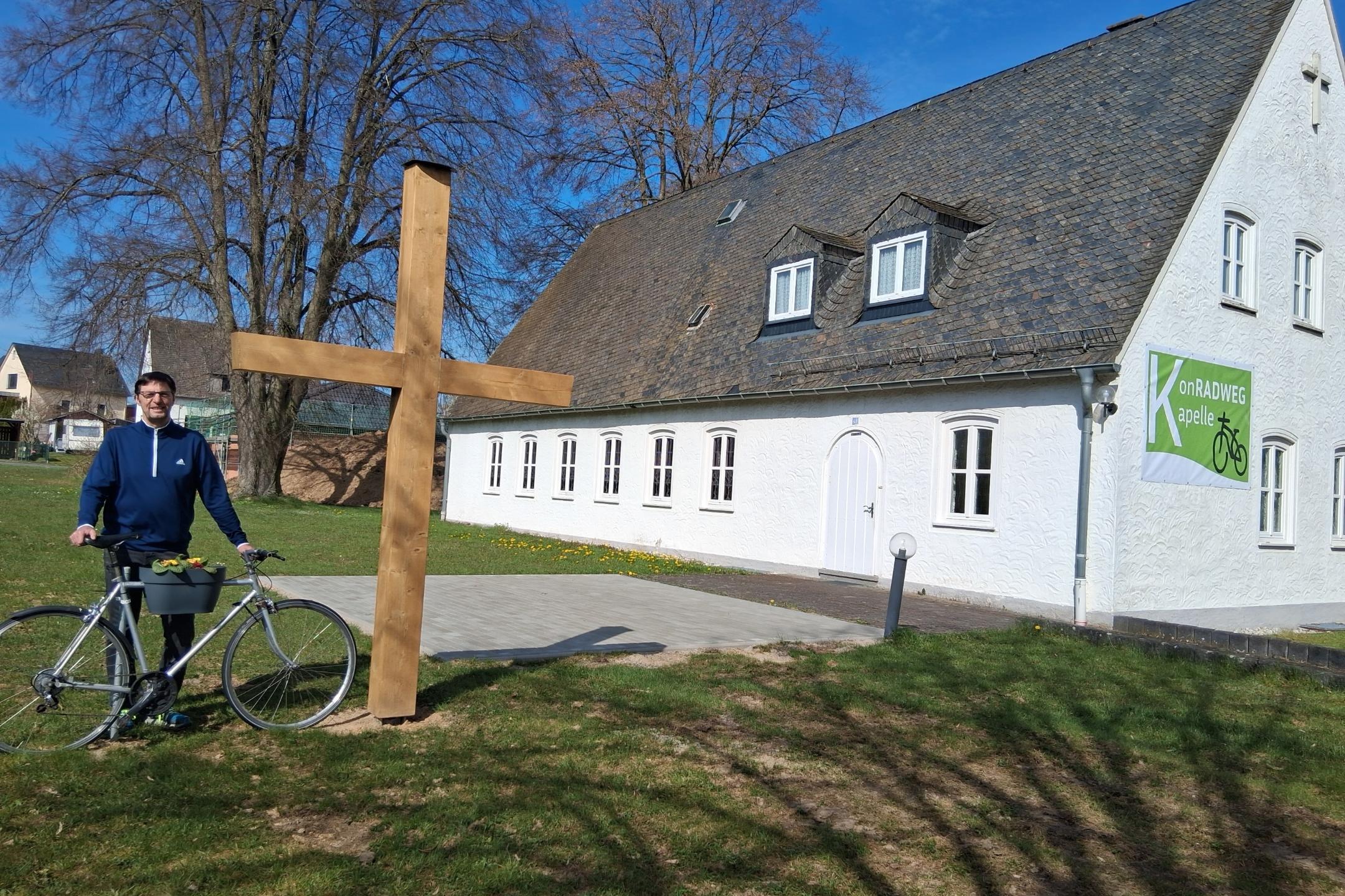 Diakon Franz Jahn mit Fahrrad bei dem neuen Holzkreuz vor der KonRADWEG-Kirche