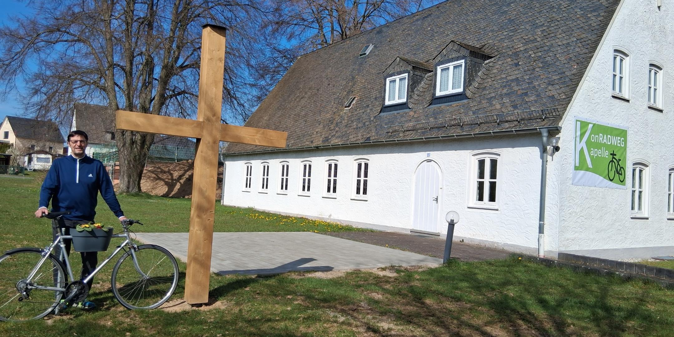 Diakon Franz Jahn mit Fahrrad bei dem neuen Holzkreuz vor der KonRADWEG-Kirche